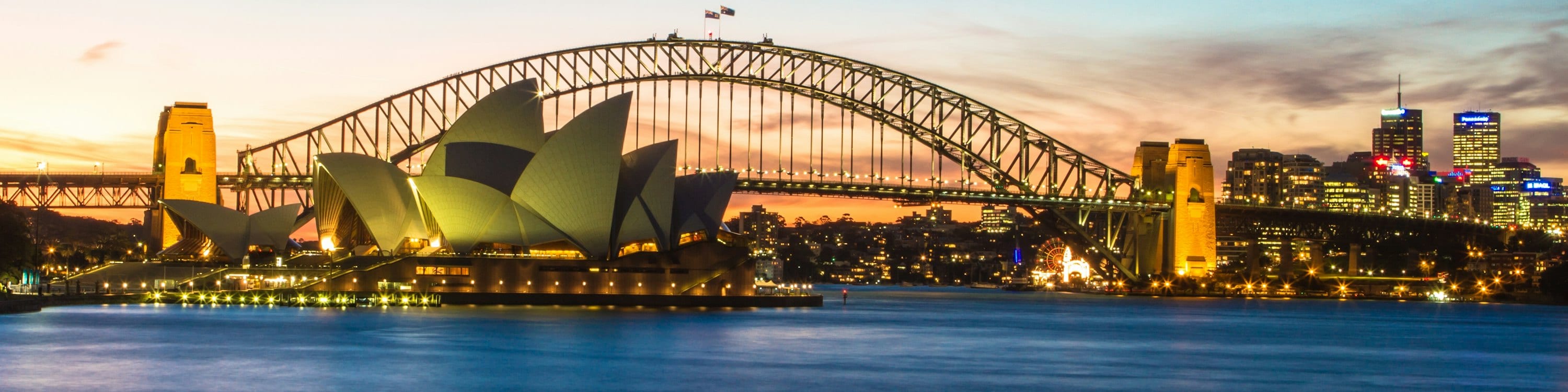Sydney Harbour at dusk from Mrs Macquarie's Chair: the Opera House and the Harbour Bridge lit against the city skyline.