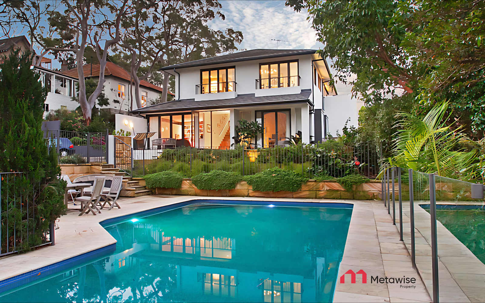 Pool and garden of the six-bedroom Mosman home in the evening, the house lit behind.